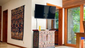 Una habitación con una televisión de pantalla plana grande montada en la pared, un tapiz estampado, un mueble decorativo y un cuenco de flores sobre un felpudo azul.