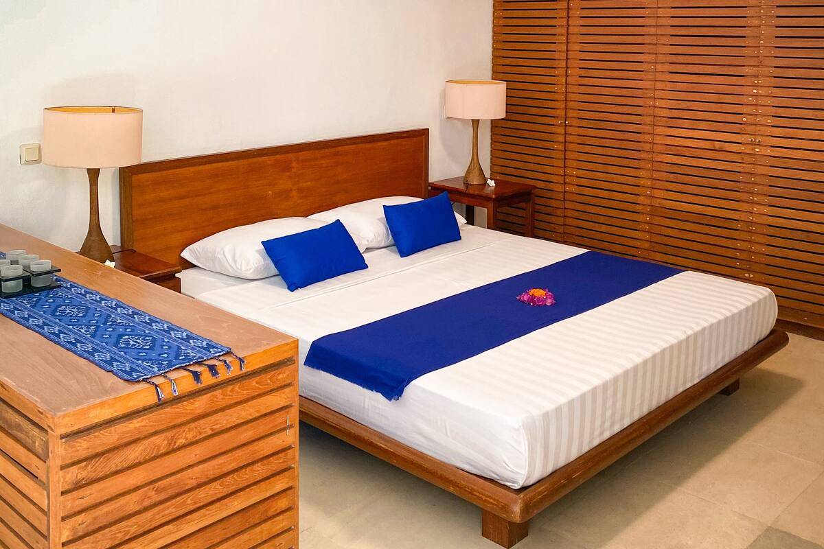 A hotel room with a wooden bed, two bedside lamps, a wooden nightstand, and a blue patterned runner.