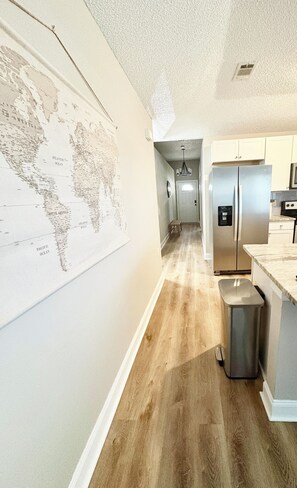 A kitchen with a stainless steel refrigerator, a wooden floor, and a map on the wall. - Cozy Hideaway! Spacious and centrally located. Pet Friendly! (Pensacola)