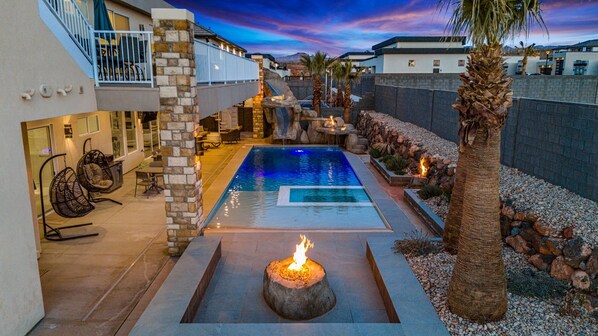 A modern outdoor pool area with a stone fire feature, seating, and a view of the surrounding neighborhood.