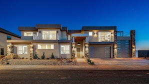 A modern two-story house with a garage, stone accents, and a well-lit entrance. - Pecan Valley Resort| BRAND NEW Private Pool and Hot Tub w/ Slide (Hurricane)