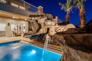A swimming pool with a waterfall feature, surrounded by large rocks and palm trees.