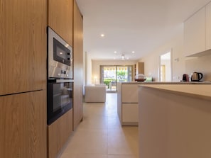 A modern kitchen with wooden cabinets, a built-in oven, and a large island with a kettle.