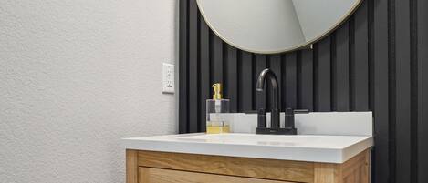 A bathroom with a wooden vanity, a round mirror, and a modern faucet.