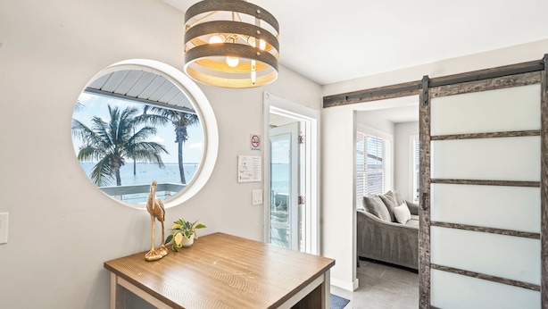 A room with a wooden table, a round mirror, and a view of palm trees through a window. - Banana River Resort (Patrick Air Force Base)