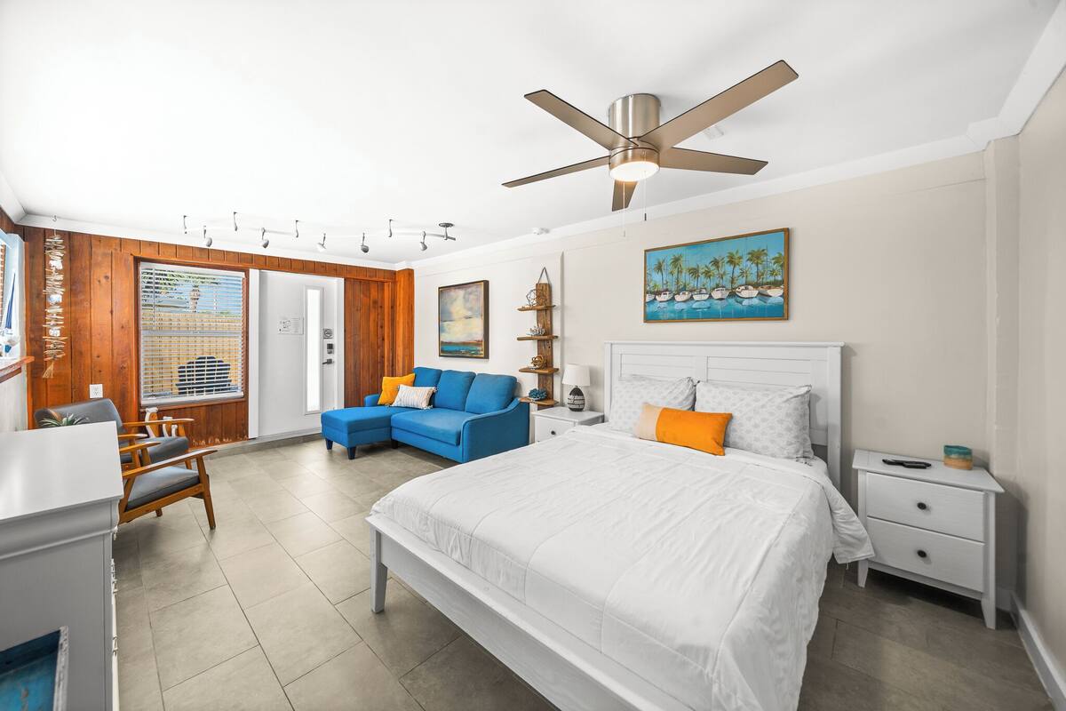 A bedroom with a large bed, a ceiling fan, a blue sofa, and a wooden wall panel.