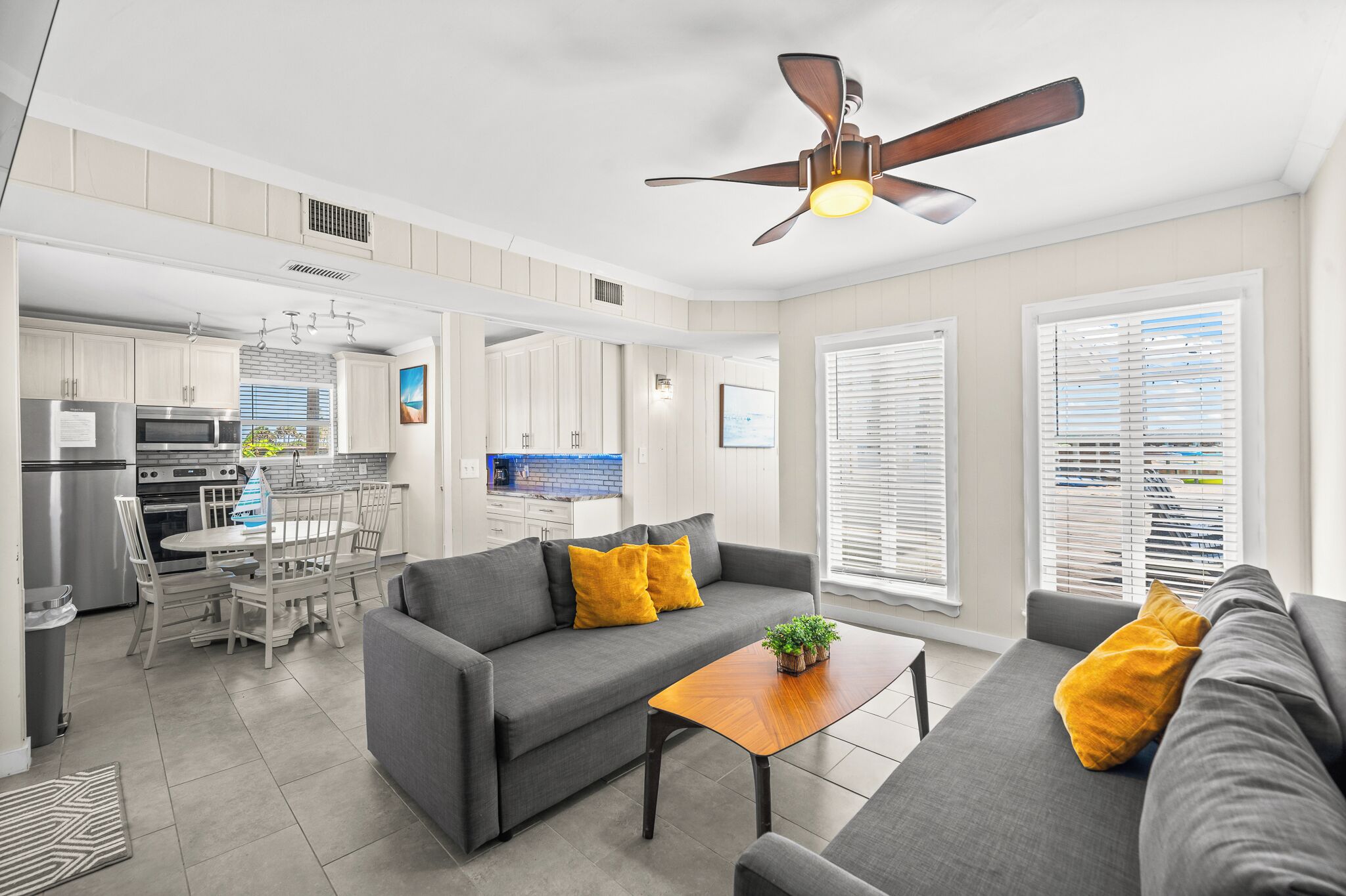 A modern kitchen with a dining area, a gray sofa, and a ceiling fan.