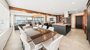 A modern kitchen with a central island, dining area with white chairs, and a view of the ocean through large windows. - Banana River Resort (Patrick Air Force Base)
