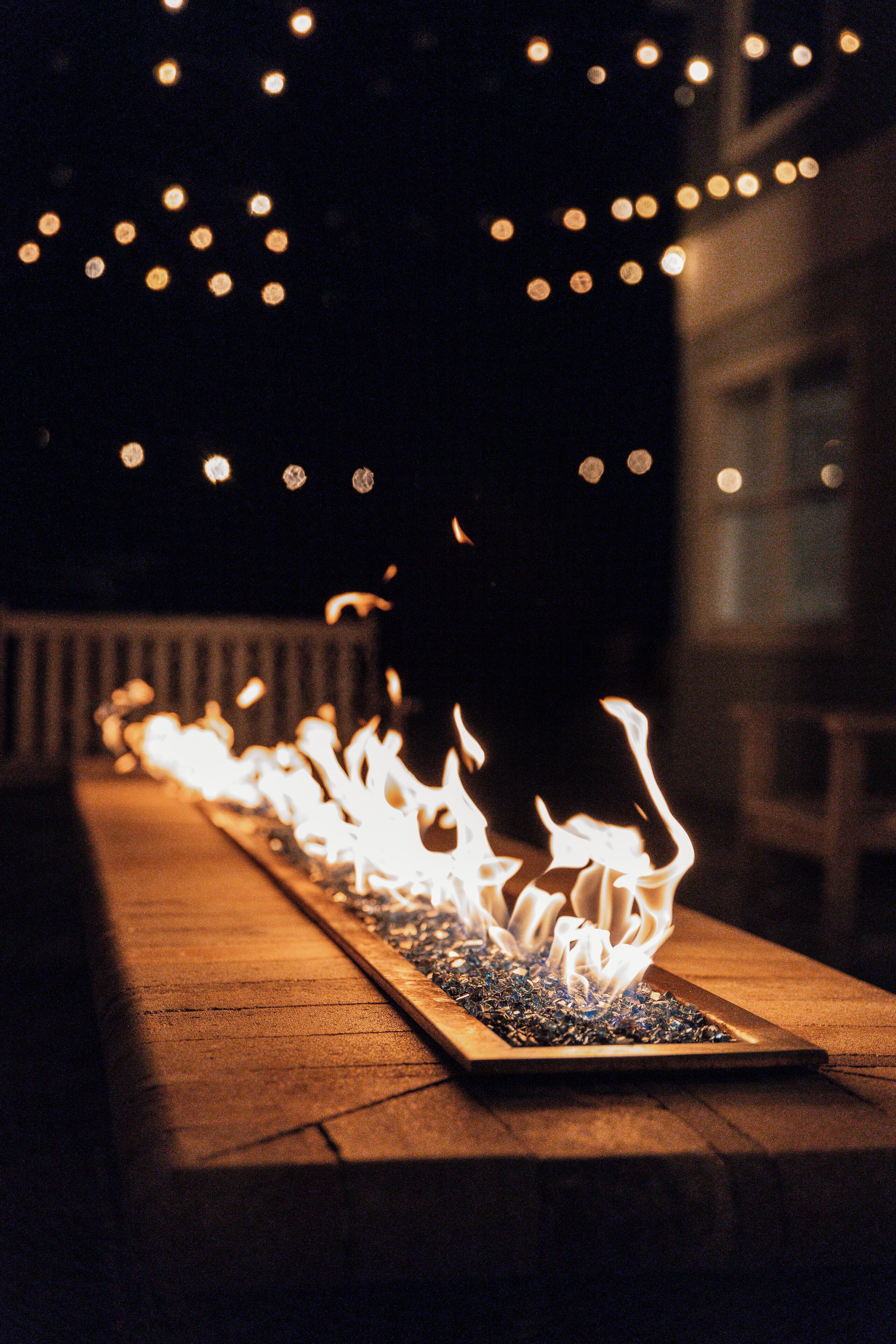 A row of flames on a long table, with string lights in the background.