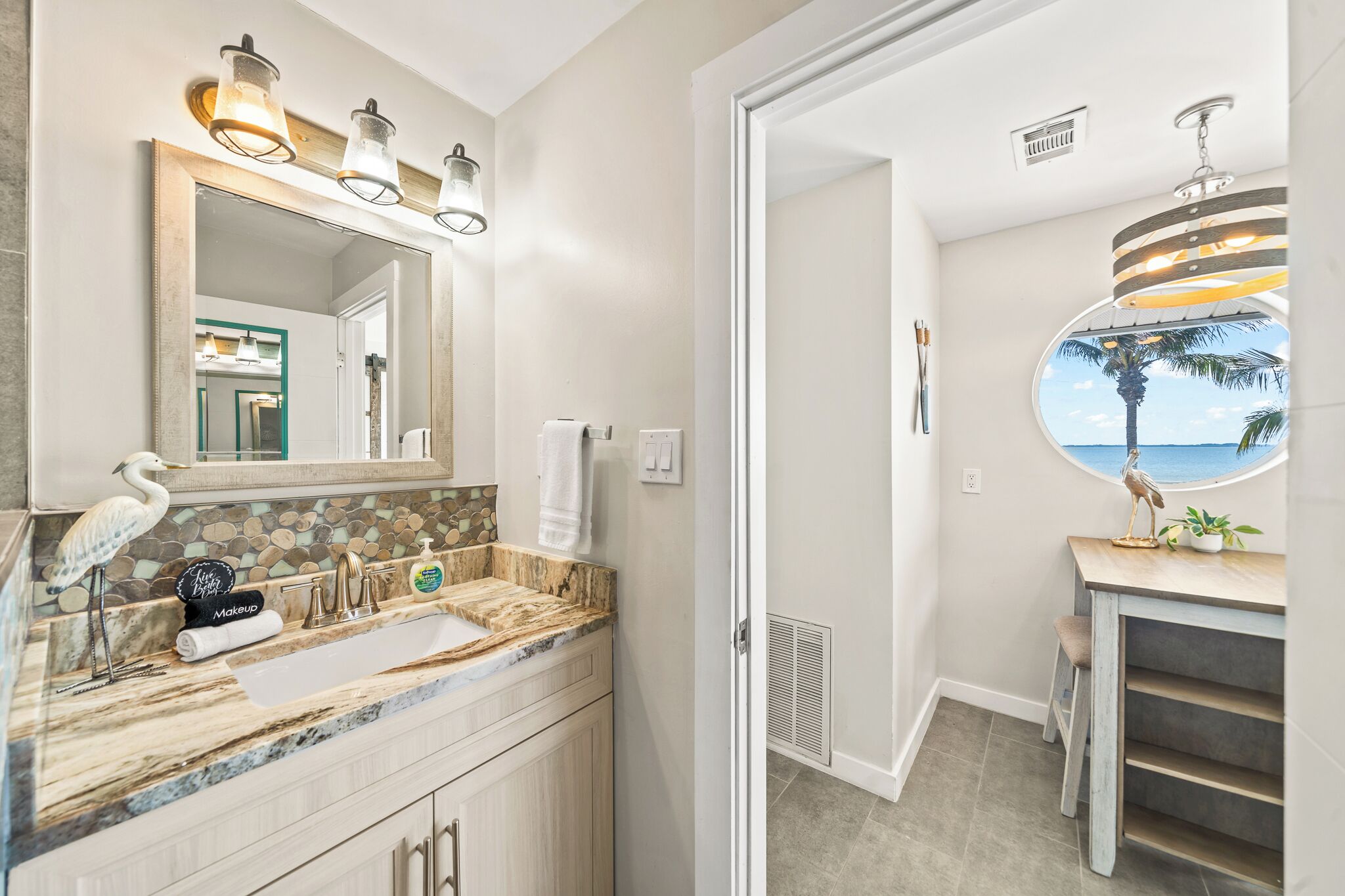 A bathroom with a vanity, a large mirror, and a view of the ocean through a circular window.