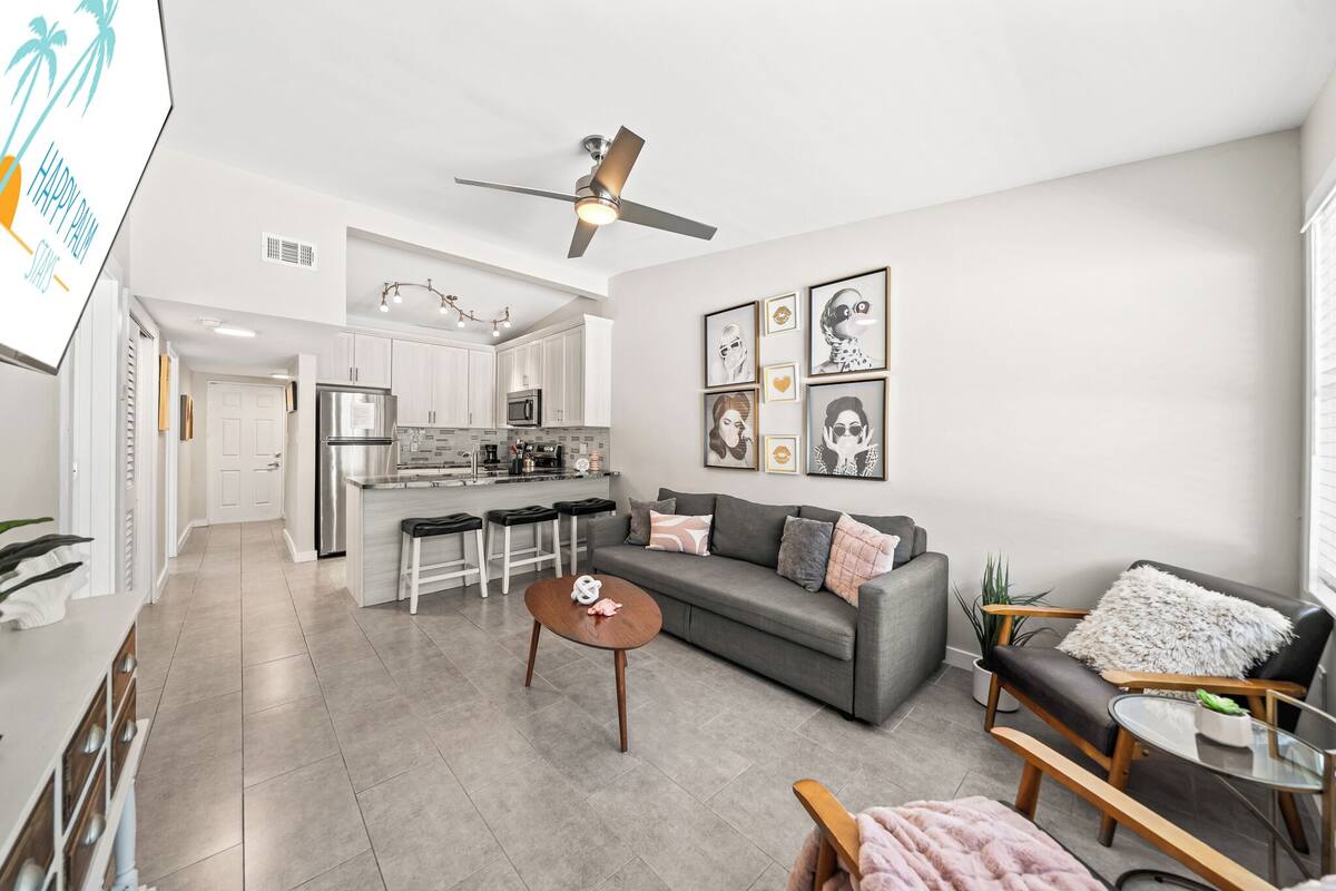 A modern living room with a grey sofa, a coffee table, and a dining area with white cabinets and a kitchen in the background.