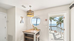 A room with a wooden desk, a round mirror, and a view of a balcony with a railing and palm trees. - Banana River Resort (Patrick Air Force Base)