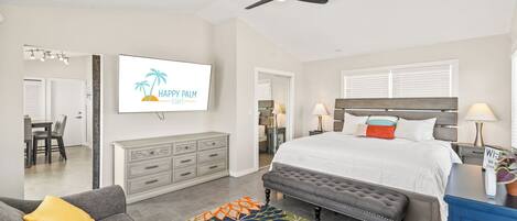 A spacious bedroom with a large bed, a ceiling fan, a TV, and a desk area.
