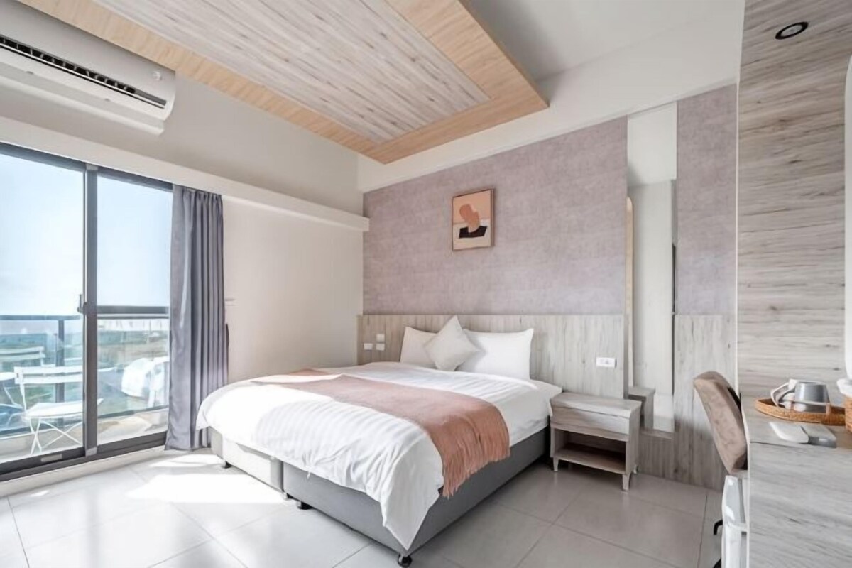 A modern hotel room with a large bed, a bedside table, a chair, and a view of the city.
