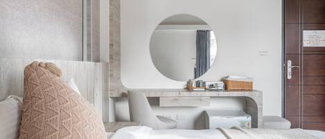 A modern bedroom with a large bed, a round mirror, a wooden dresser, and a door with a sign.