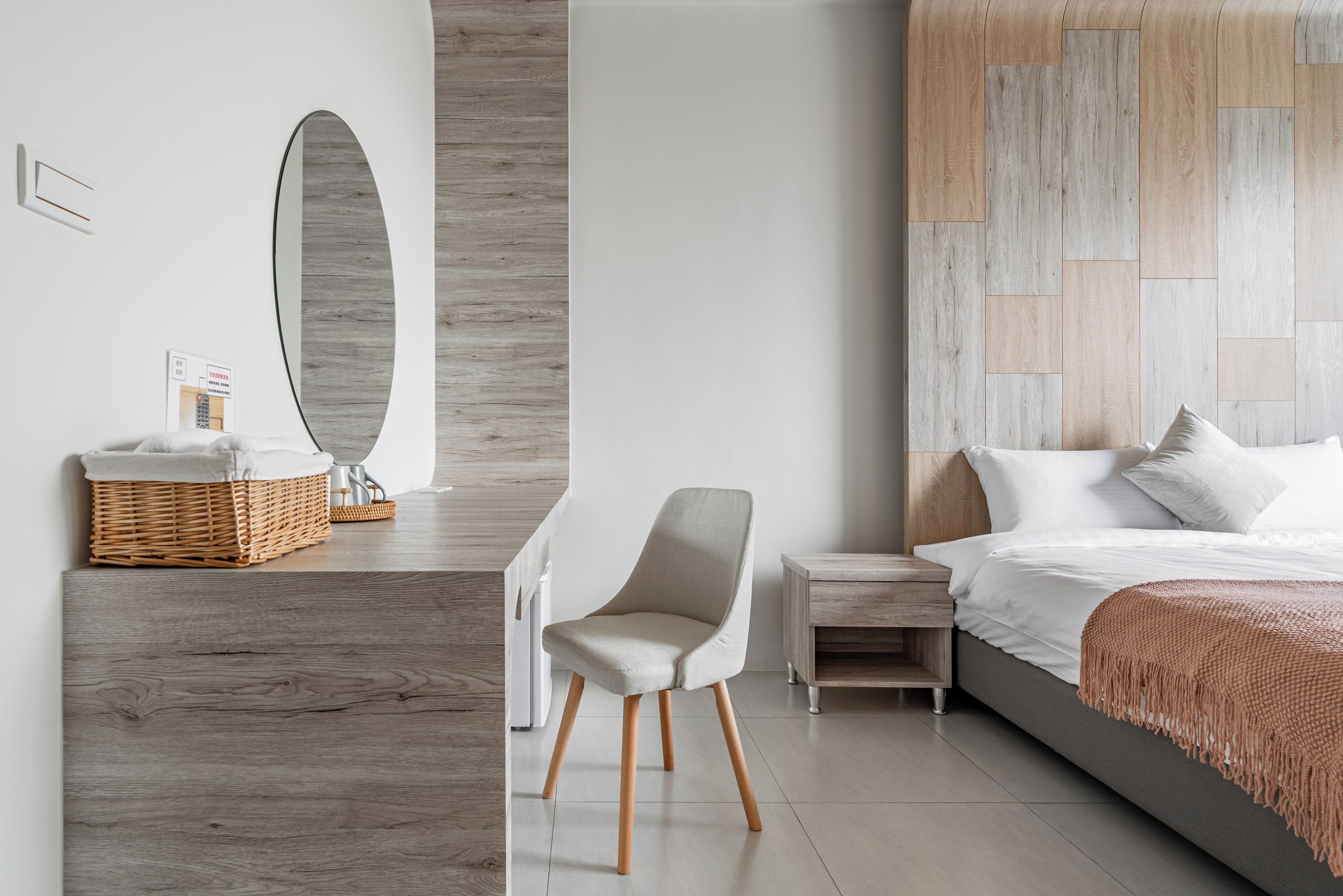 Un dormitorio moderno con cabecera de madera, una mesita de noche, una silla y una cama con ropa blanca de cama.