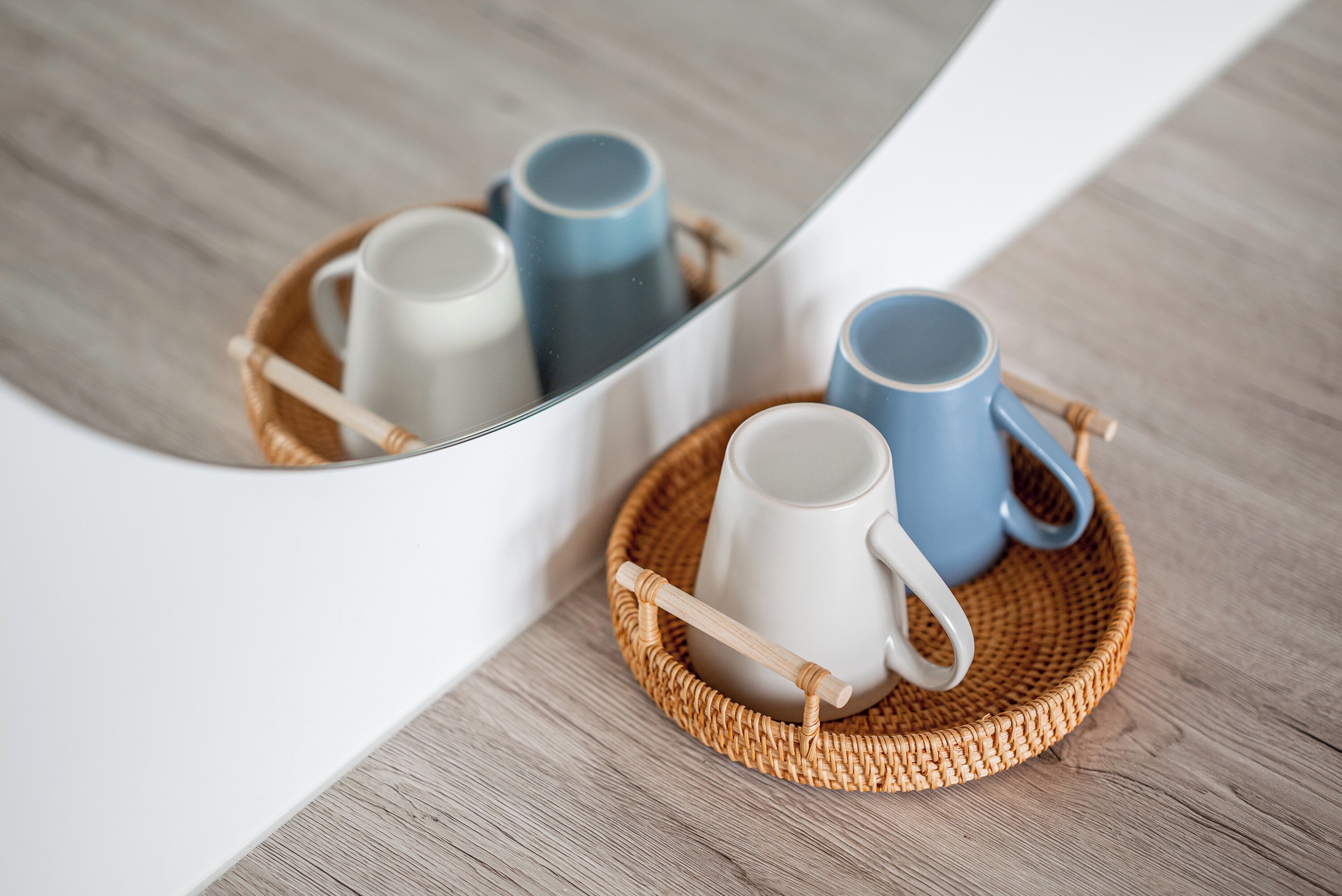 A mirror reflecting two mugs on a woven tray.