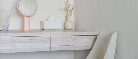 Un tocador minimalista con superficie de madera, espejo rosa, caja de pañuelos blancos y un florero con plantas secas.