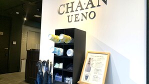 A wall with 'CHAAN UENO' signage, a drink server with instructions, and a display of umbrellas. - CHA-AN UENO (Tokyo)