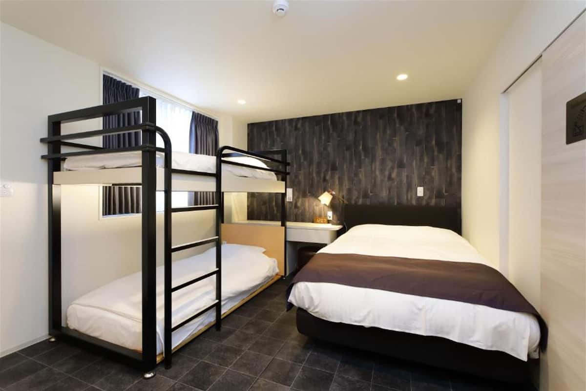 Une chambre avec deux lits superposés, un lit simple, une table de chevet avec une lampe et un mur recouvert de panneaux en bois foncé.