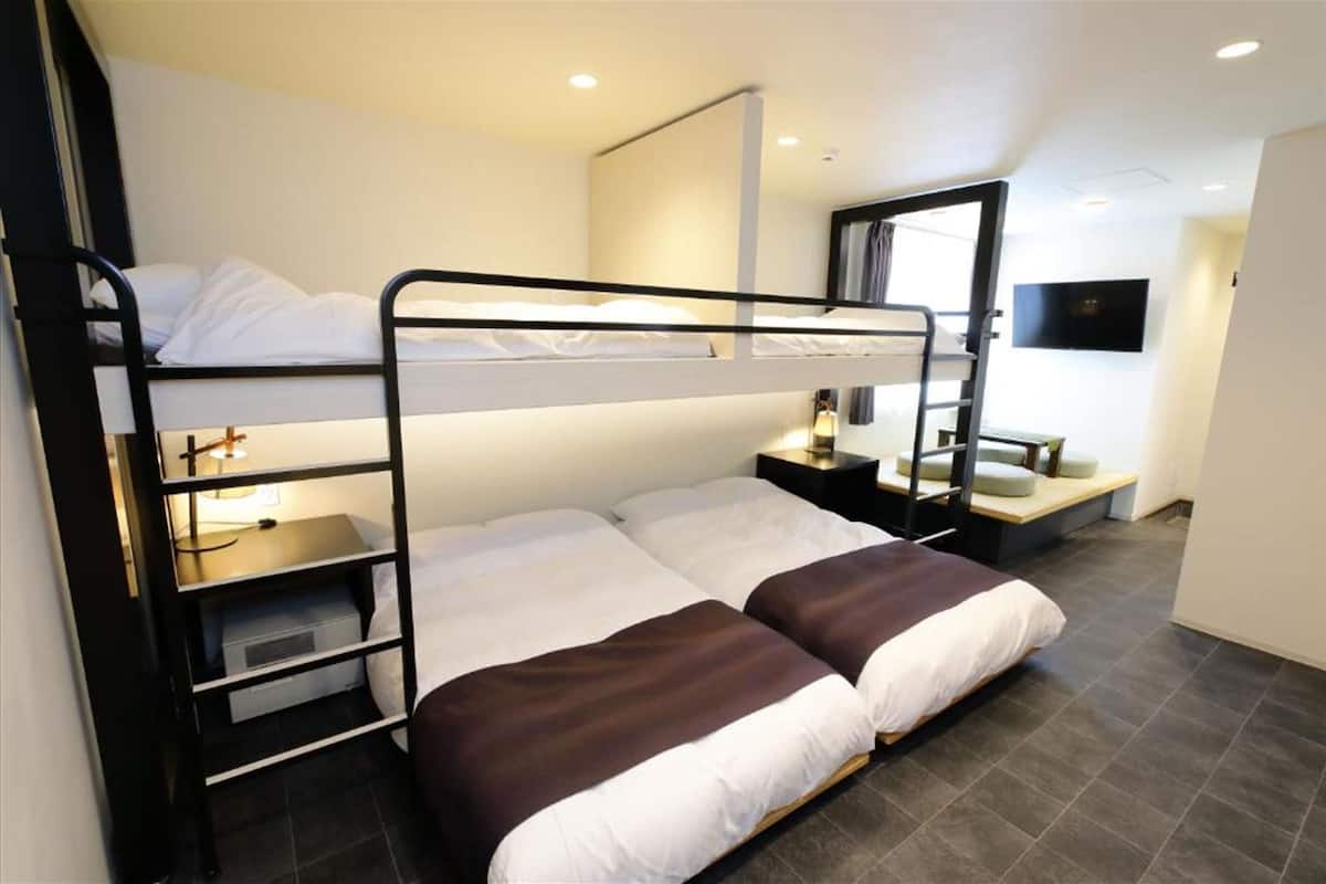 Une chambre avec un lit superposé, un bureau et une chaise, un miroir et un téléviseur fixé au mur.