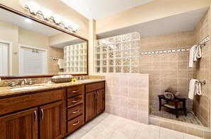 Un baño con tocador de madera, un espejo grande, ducha con paneles de vidrio y suelo de baldosas.
