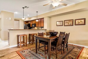 Un comedor con mesa y sillas de madera, una cocina con armarios de madera, luces colgantes y un ventilador de techo.