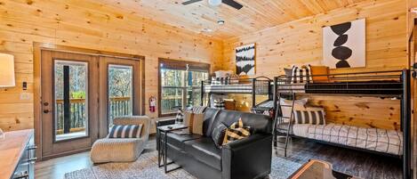 L’intérieur chaleureux d’un chalet avec un canapé en cuir noir, une table à manger en bois et un lit superposé.
