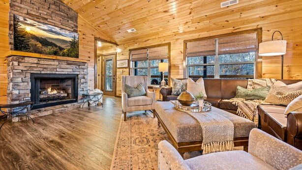 Un intérieur de chalet chaleureux avec une cheminée en pierre, un plafond en bois et de grandes fenêtres.