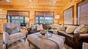 L’intérieur chaleureux d’un chalet avec des murs en bois, un canapé en cuir, un fauteuil assorti et une table basse agrémentée d’un élément décoratif.