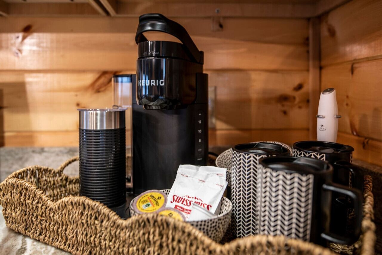 Une petite cuisine équipée d’une machine à café Keurig, d’un mousseur à lait et de divers mugs et récipients.