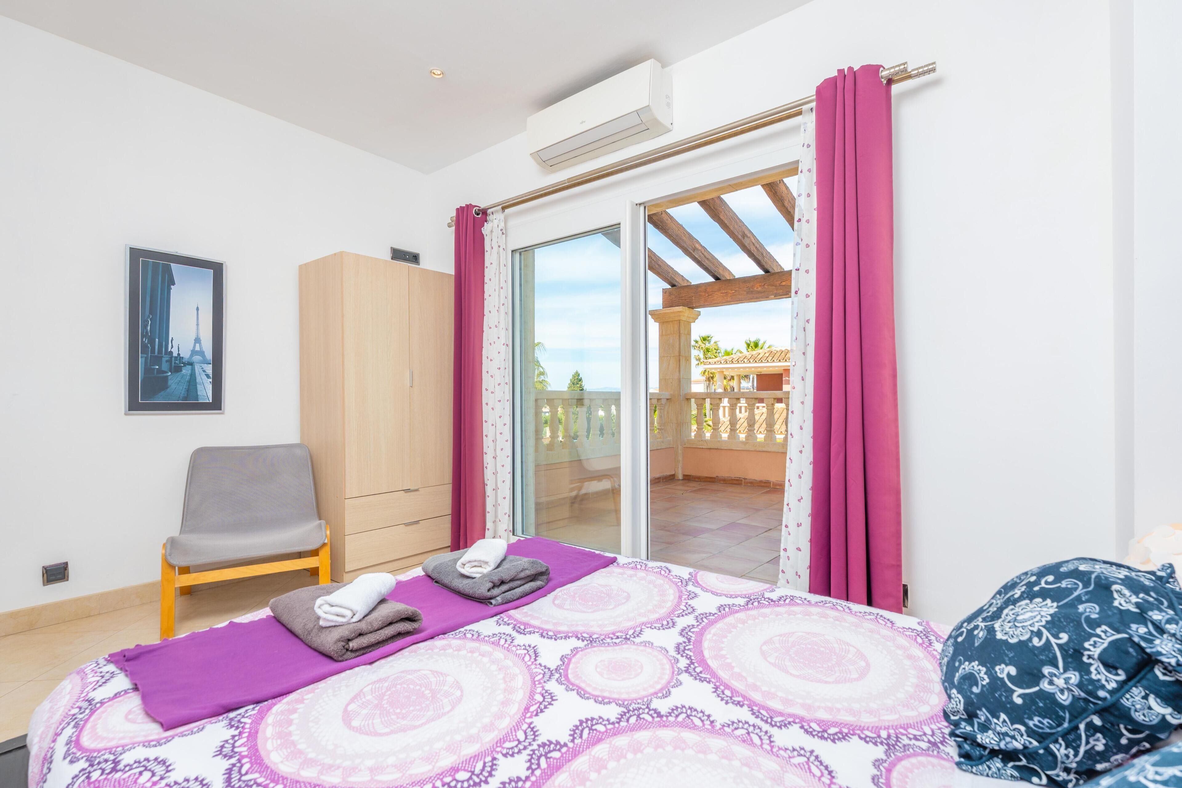 A bedroom with a bed, a chair, a wardrobe, and a sliding glass door leading to an outdoor area.