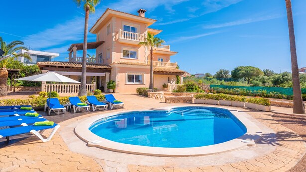 Un bâtiment à deux étages doté d’une piscine, de chaises longues et de palmiers.