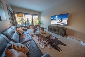 A modern living room with a leather couch, a wooden coffee table, and a large flat-screen TV mounted on the wall. - Pines 2050 (Keystone)