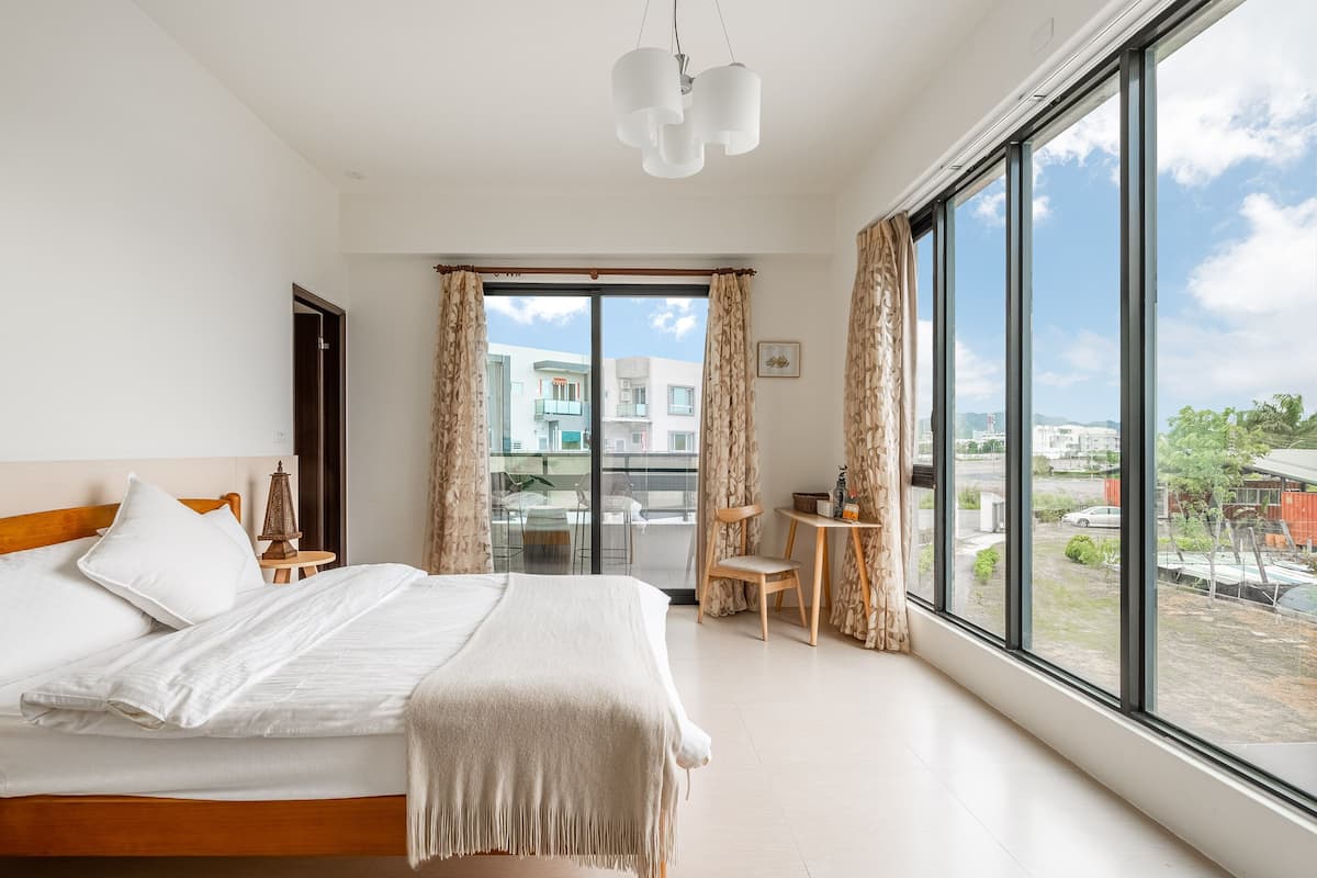 Ein modernes Hotelzimmer mit einem großen Bett, einem kleinen Tisch und Blick auf die Stadt durch große Fenster.