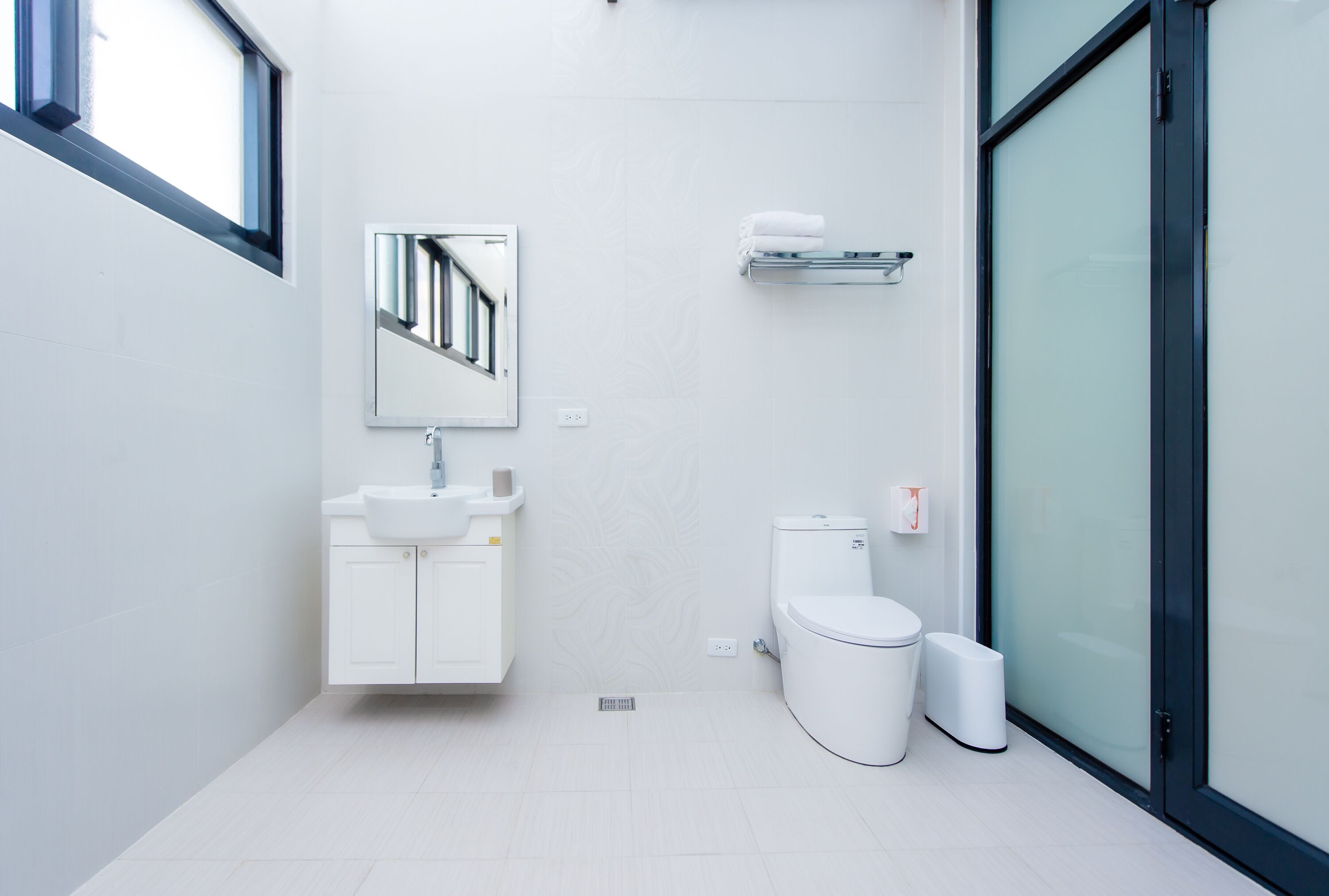 A modern bathroom with a white sink, mirror, toilet, and glass shower enclosure.