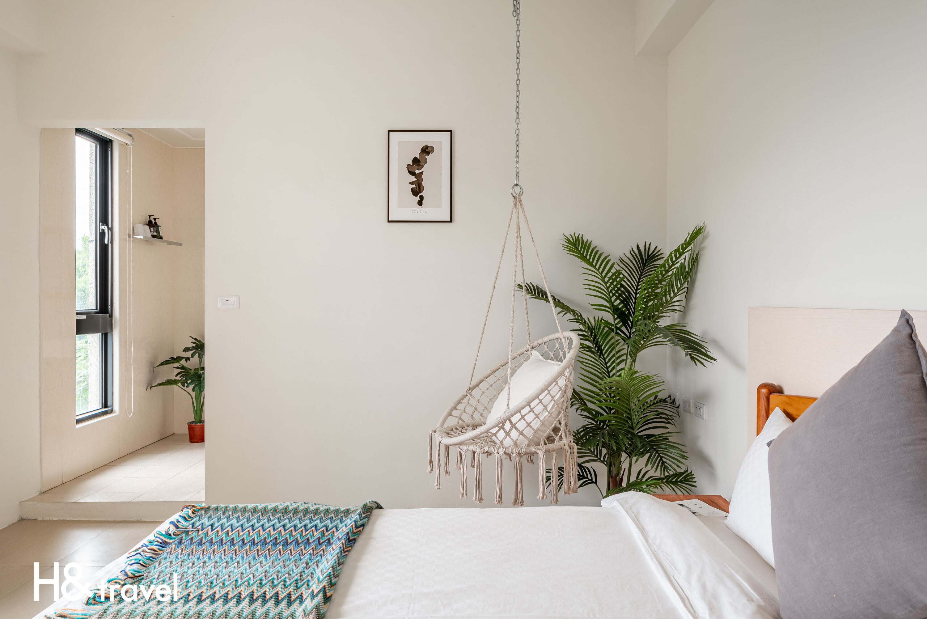Une chambre à coucher avec un lit, un fauteuil suspendu, une plante en pot et un tableau encadré au mur.
