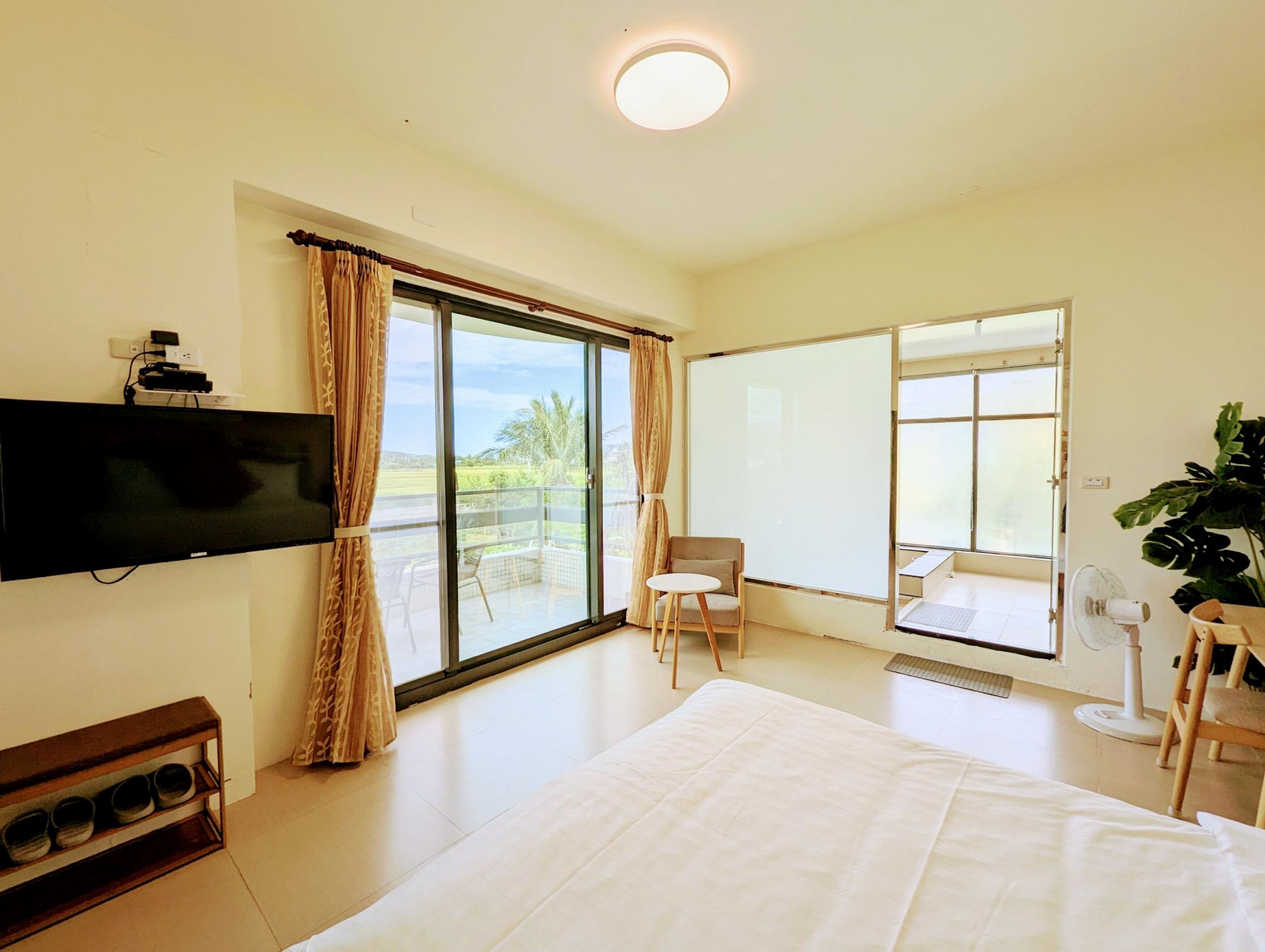 A hotel room with a large bed, a flat-screen TV mounted on the wall, a sliding glass door to the balcony, and a small table with a chair.