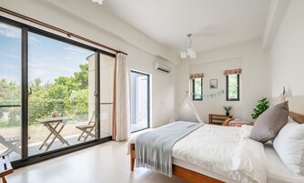 Un dormitorio con un amplio ventanal corredera que da a un espacio exterior, una cama con ropa blanca, una mesita pequeña y una lámpara colgante.