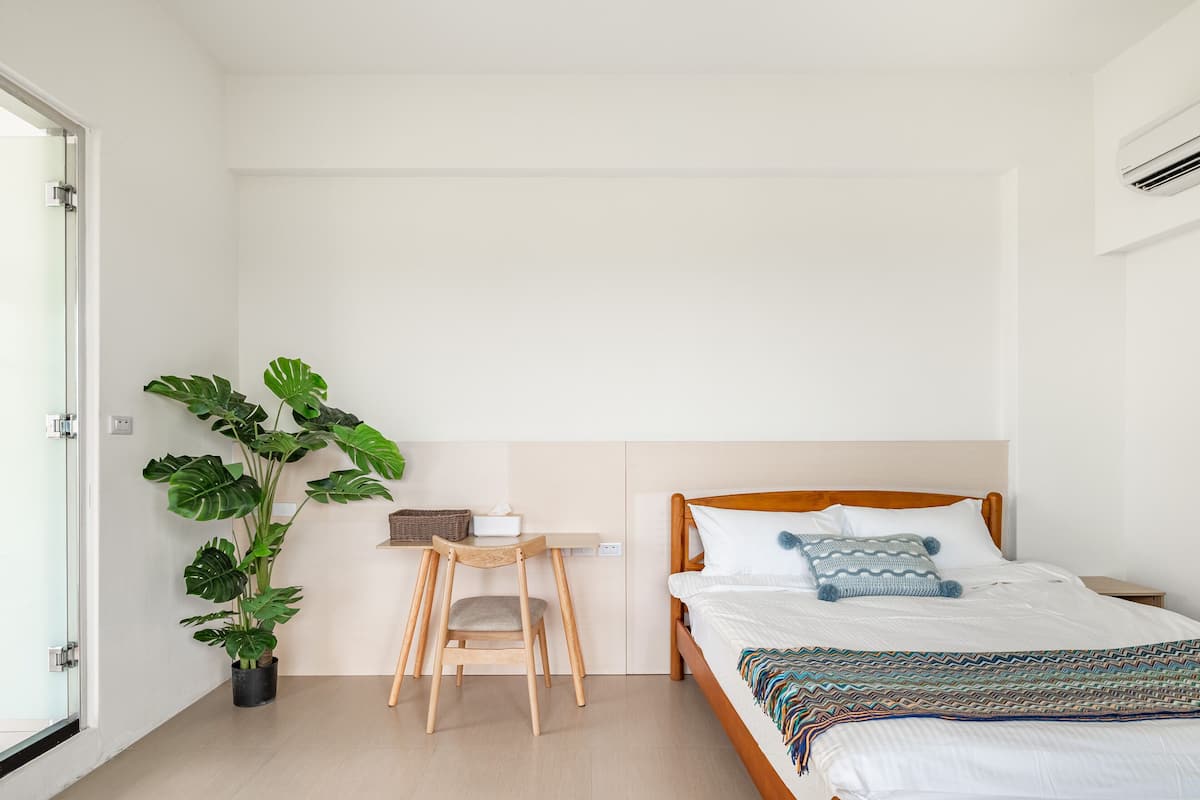 Ein Schlafzimmer mit einem Bett, einem Nachttisch, einem Stuhl, einer Topfpflanze und einem Fenster.