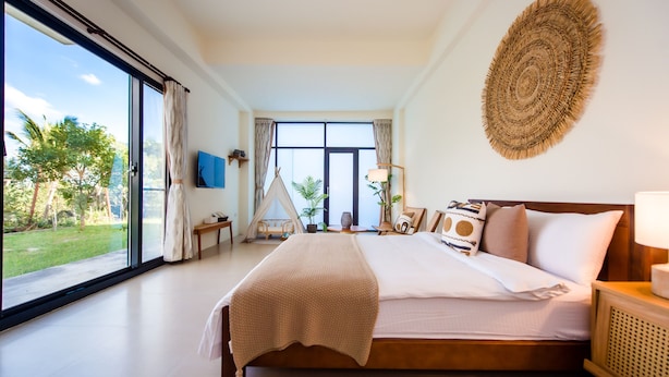 Een ruime slaapkamer met een groot bed, uitzicht op de omgeving en een wandkunstwerk van geweven materiaal.