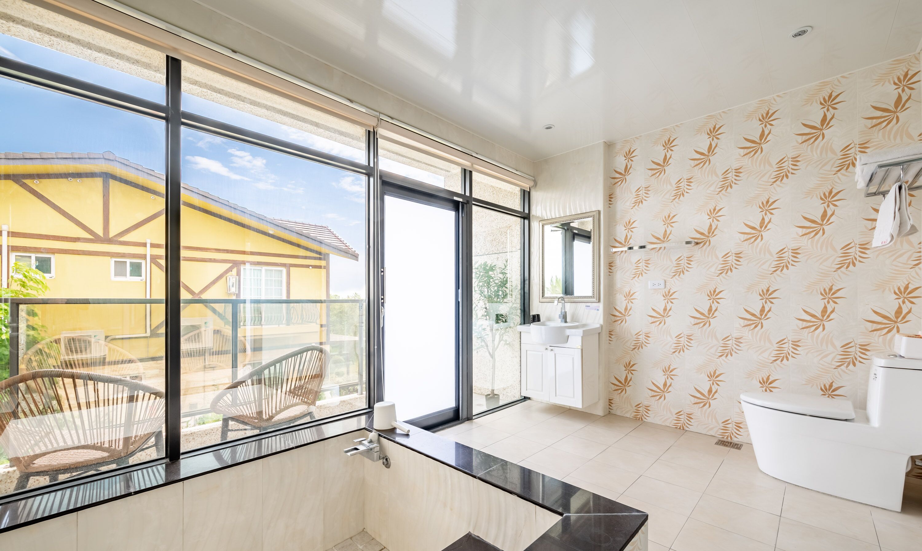 A modern bathroom with large windows, a view of a yellow building, and a toilet with a towel rack.