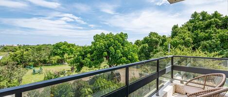 A balcony with a glass railing overlooking a lush garden and trees.