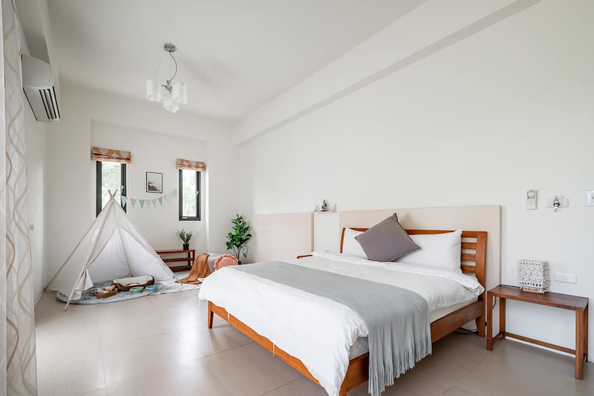 Ein Schlafzimmer mit Bett, Nachttisch, Holz-Kopfteil, Zelt und einer Pendelleuchte.