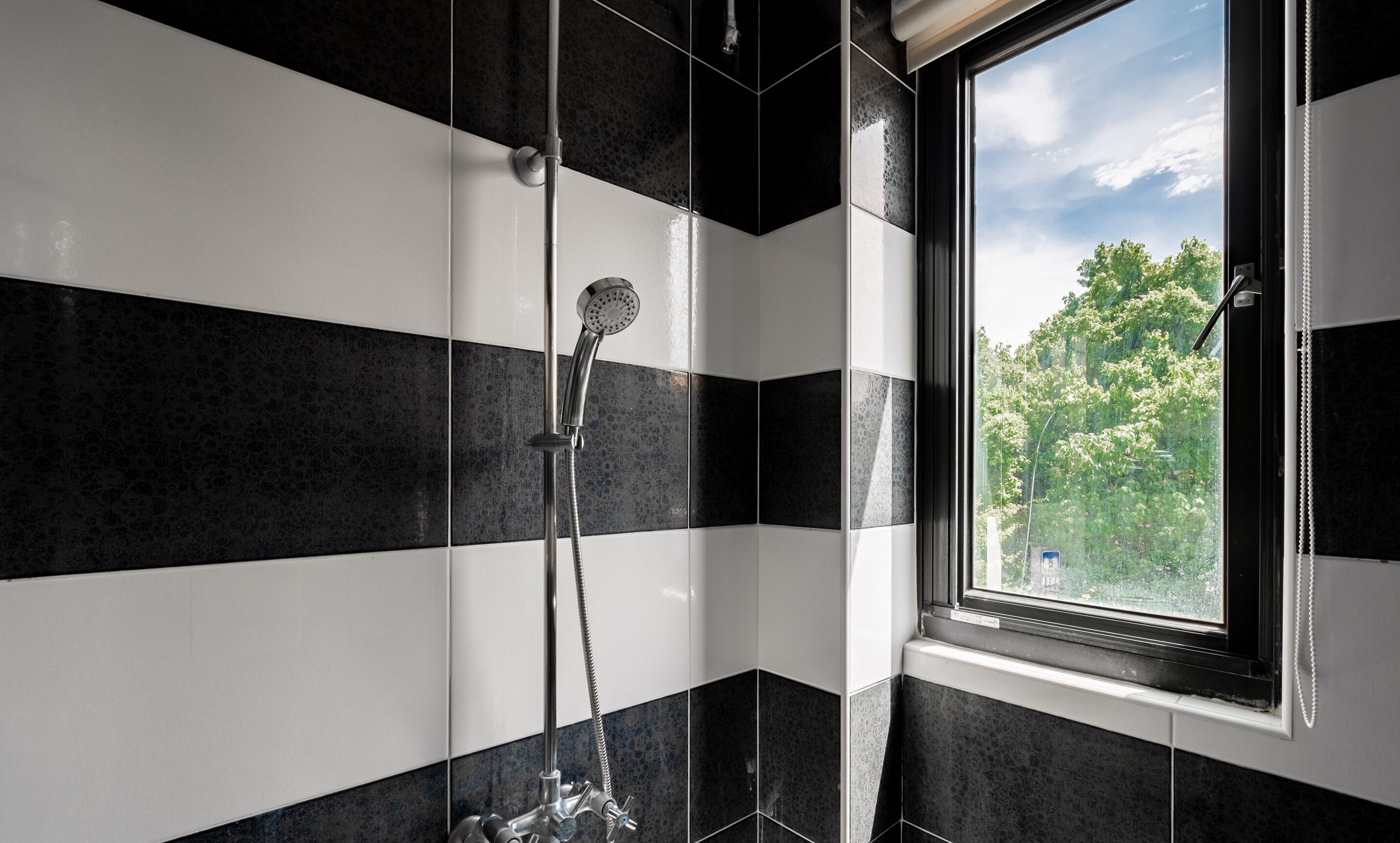 A bathroom with black and white tiles, a shower, and a window with a view of trees.