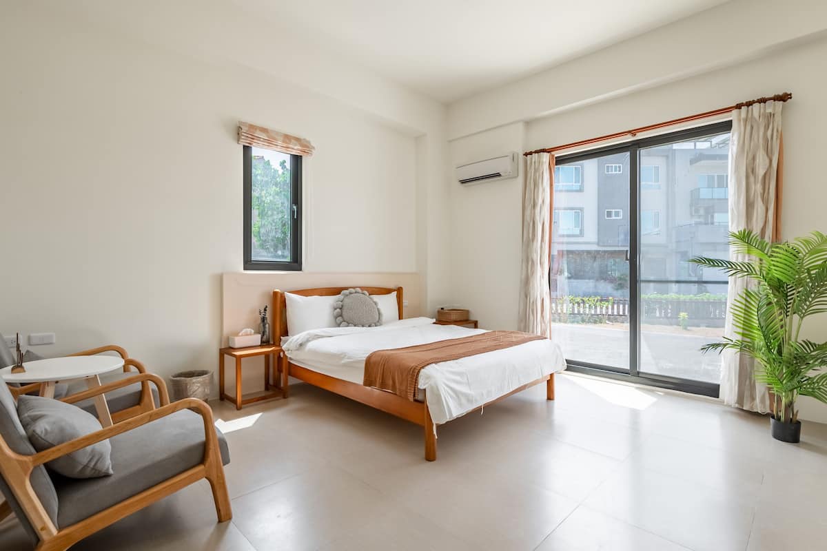 Ein modernes Schlafzimmer mit einem Bett, einem kleinen Tisch, einem Stuhl und einem Topf mit Pflanze.