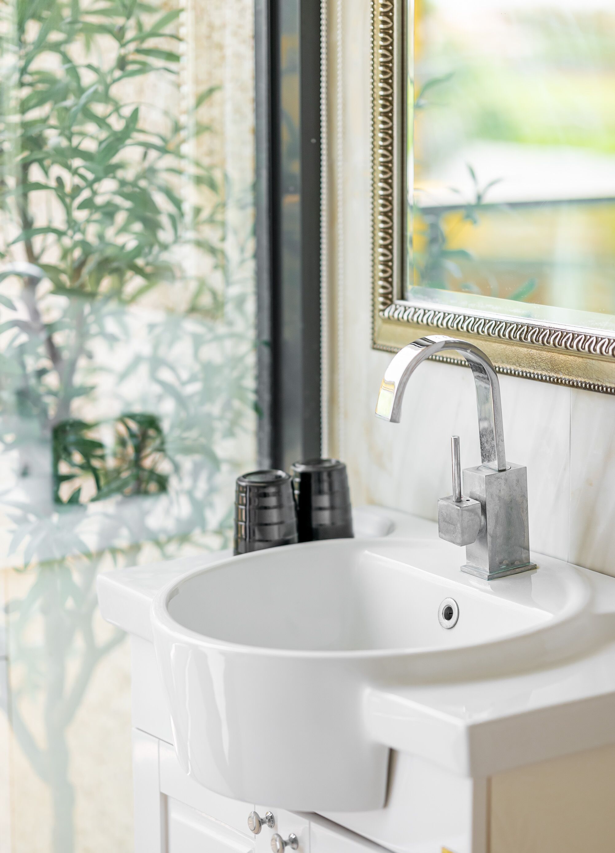 A bathroom with a white sink, a modern faucet, and a mirror with a decorative frame.