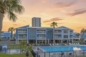 A hotel with a pool, multiple balconies, and palm trees.