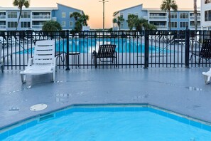 A swimming pool with lounge chairs and a fence, surrounded by buildings.