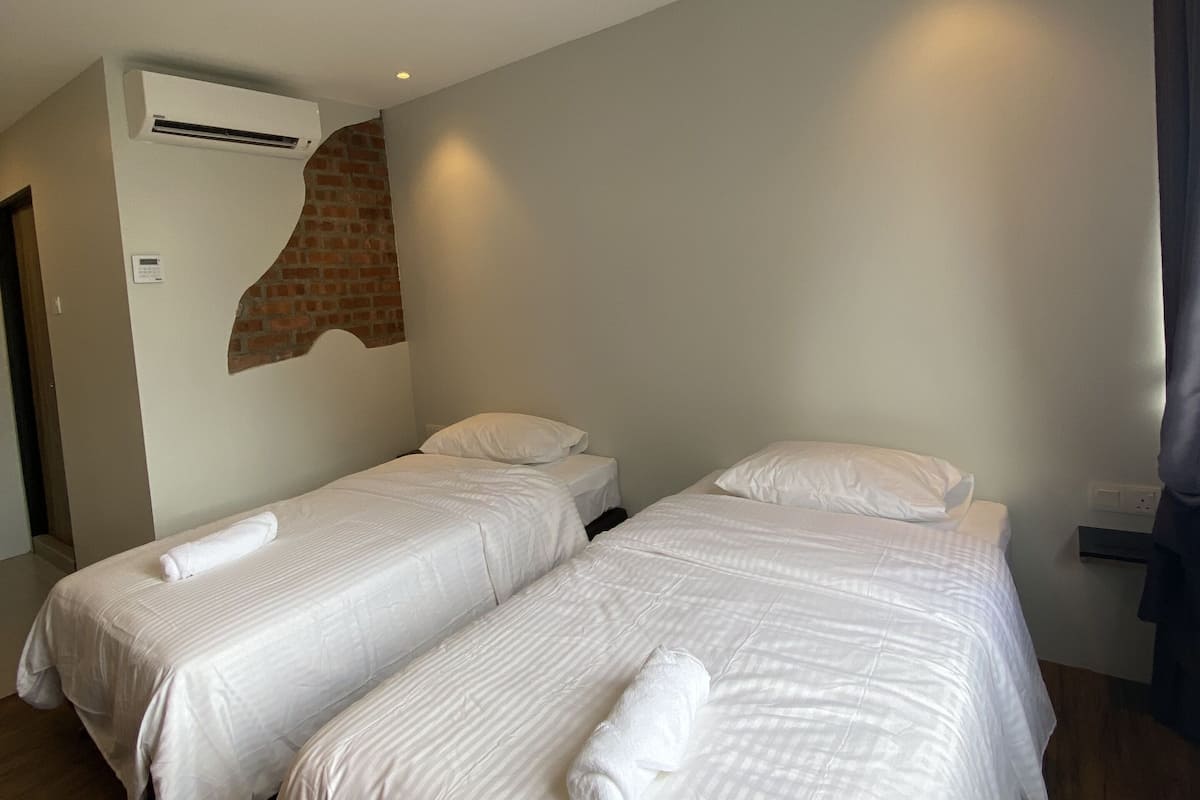 A hotel room with two single beds, an air conditioning unit, a brick accent wall, and a wooden floor.